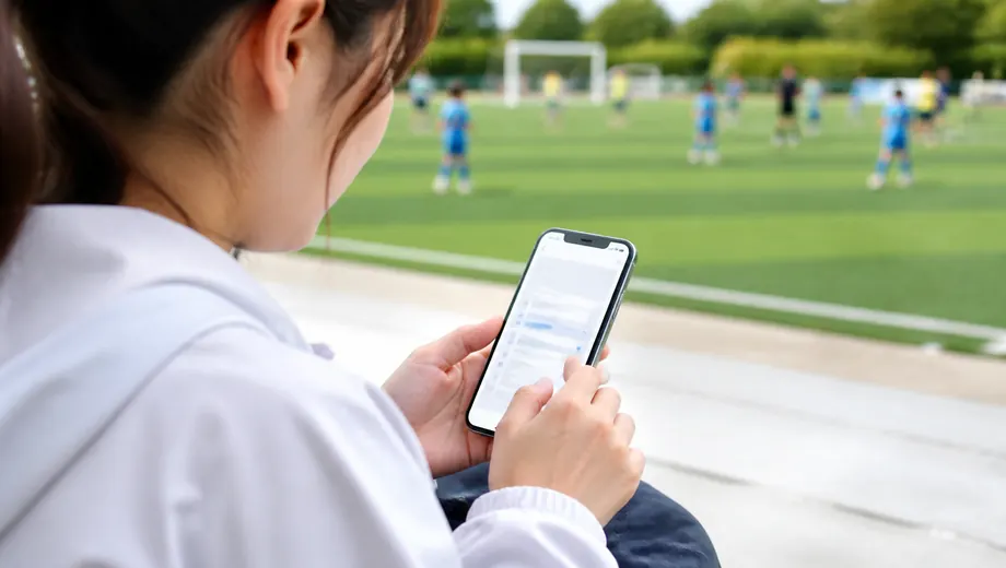 サッカー場のそばでスマートフォンから入会を申し込む保護者